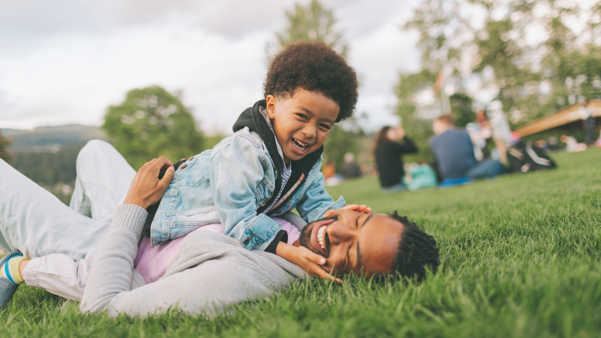 a Black man laying on the grass with a child on his chest