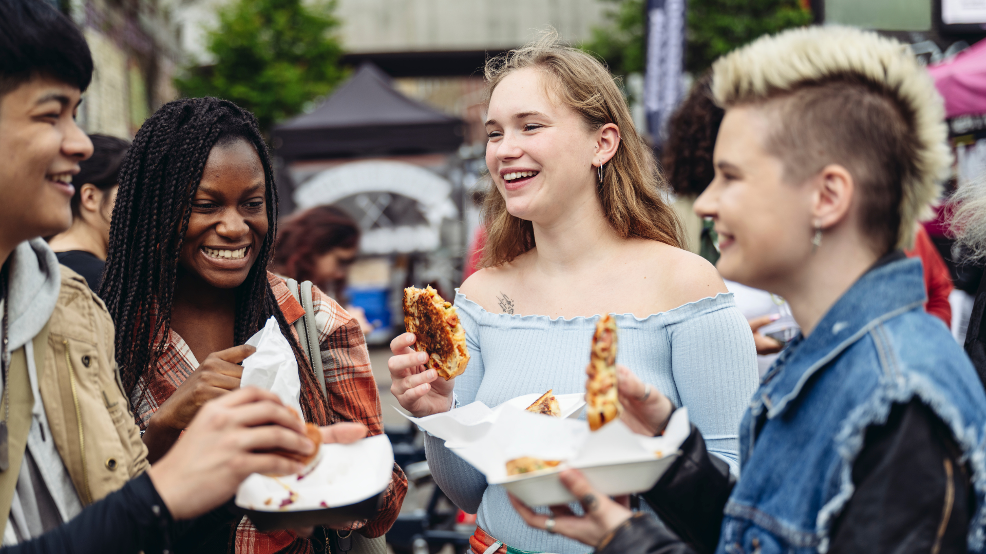 a multiracial group of young people eating chicken wings on a street