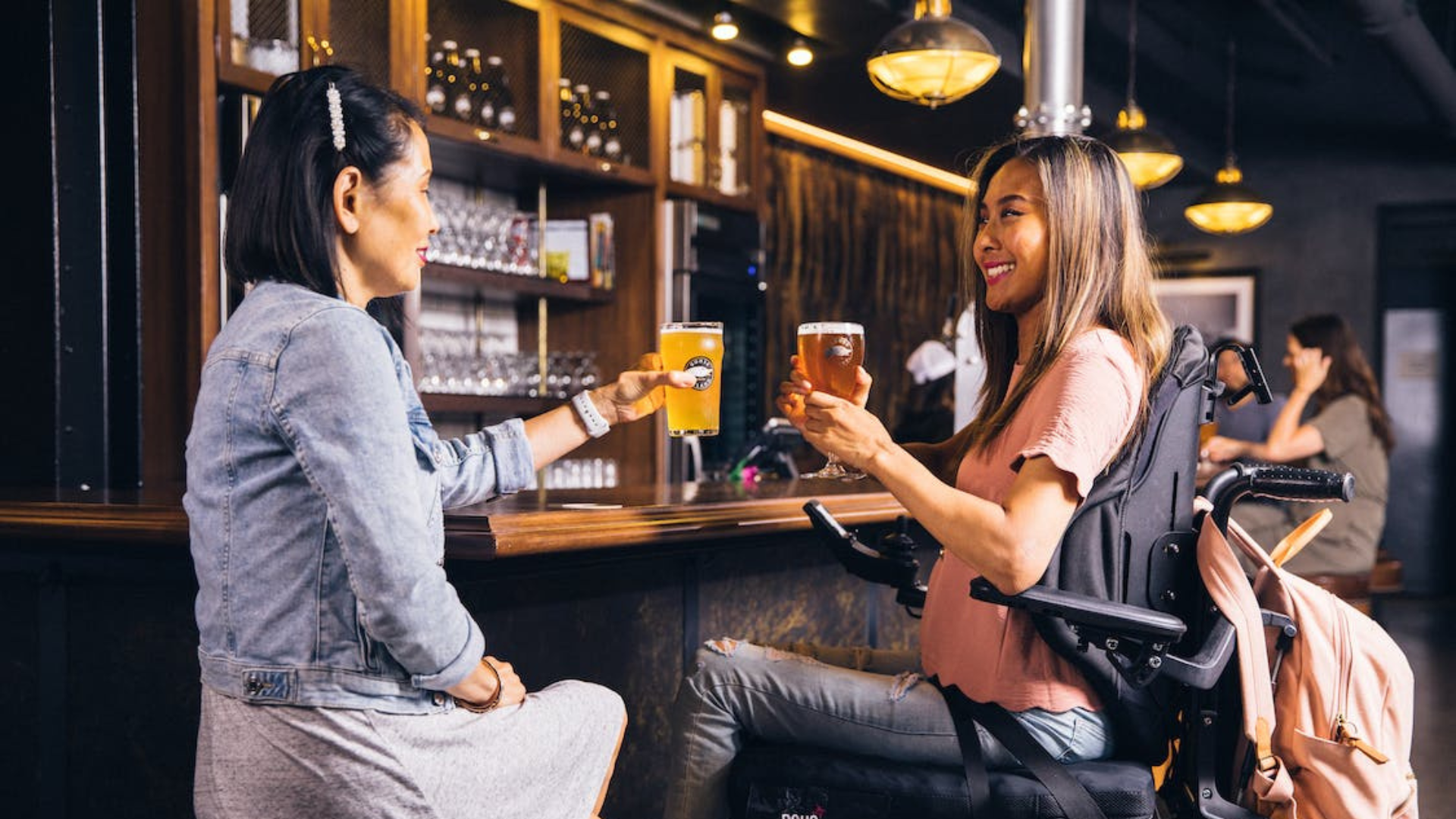 a woman in a wheelchair having a beer with her friend at a bar
